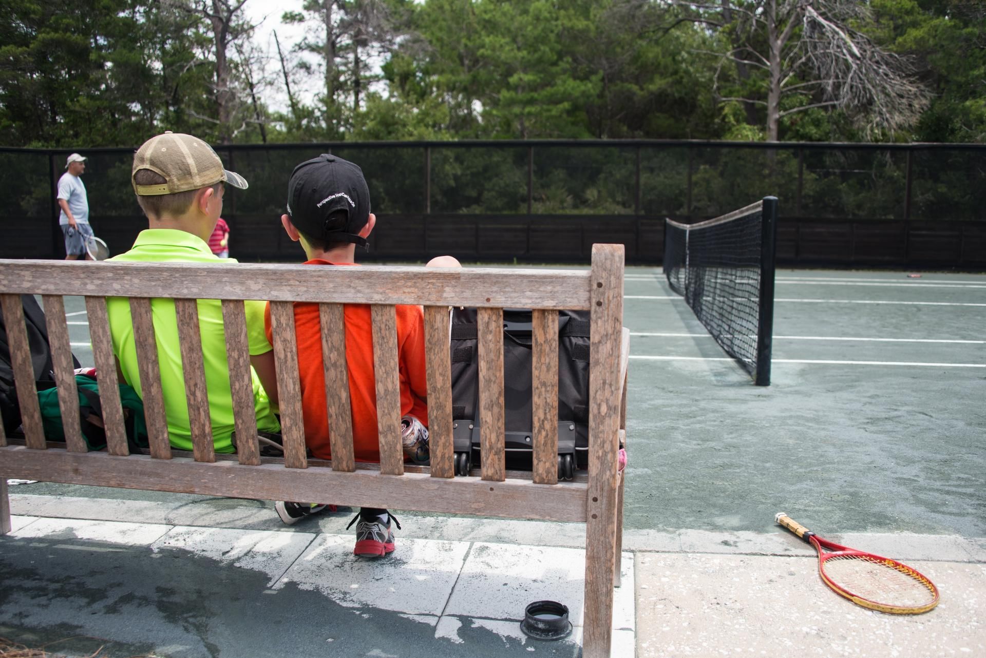 Two boys sitting on a bench by the Tennis court at Watersound Inn