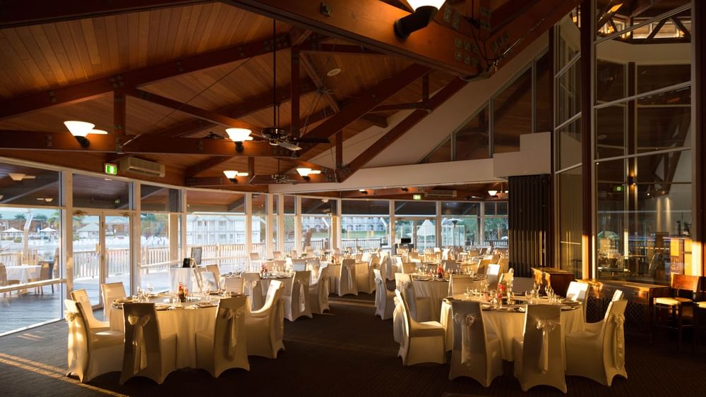 Banquets set up by large windows overlooking a waterfront in Lily’s on the Lagoon at Novotel Sunshine Coast Resort