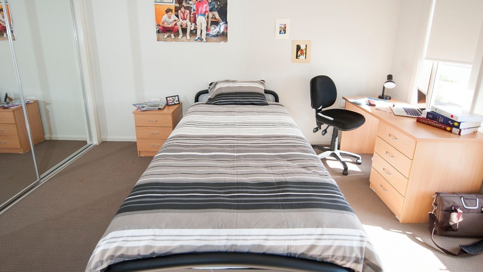 A tidy bedroom with a bed, desk, chair, and personal items at La Trobe University Regional Housing.