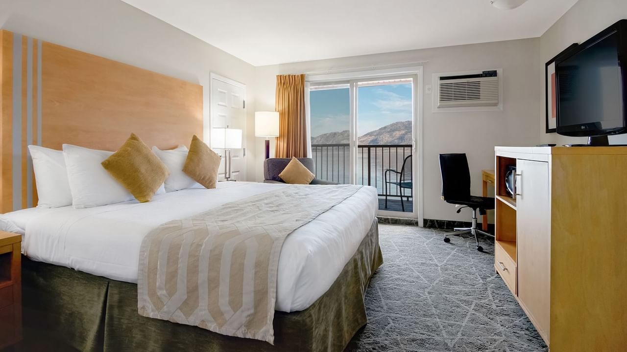 Hotel room with a king-size bed, desk, TV and lake view from the balcony.