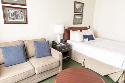 Standard Room Queen with a Tan sofa & blue pillows sits by a wooden nightstand at Rodd Charlottetown Hotel