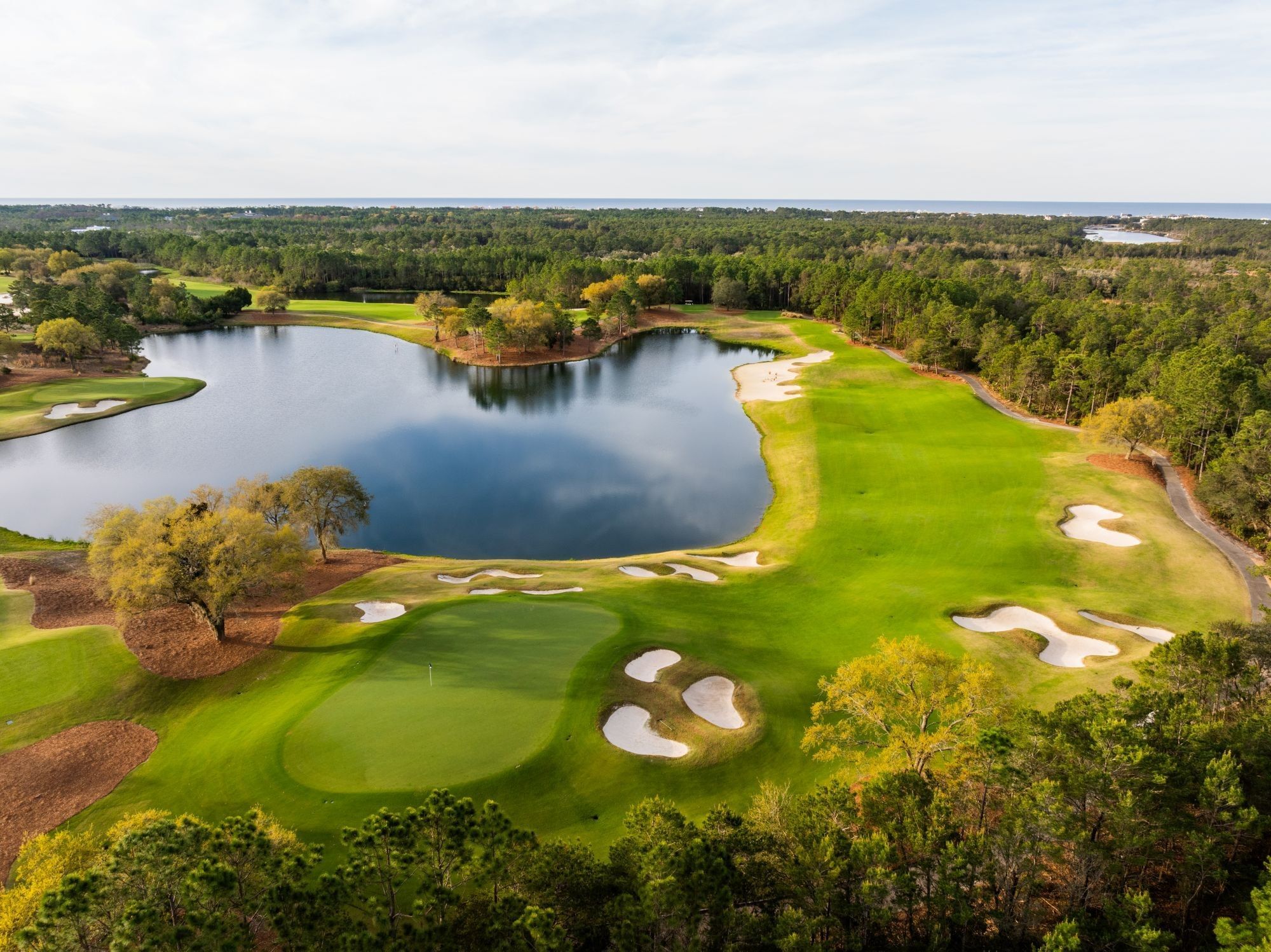 Aerial view of Camp Creek Inn's golf course with a large pond and forest surroundings at Camp Creek Inn.