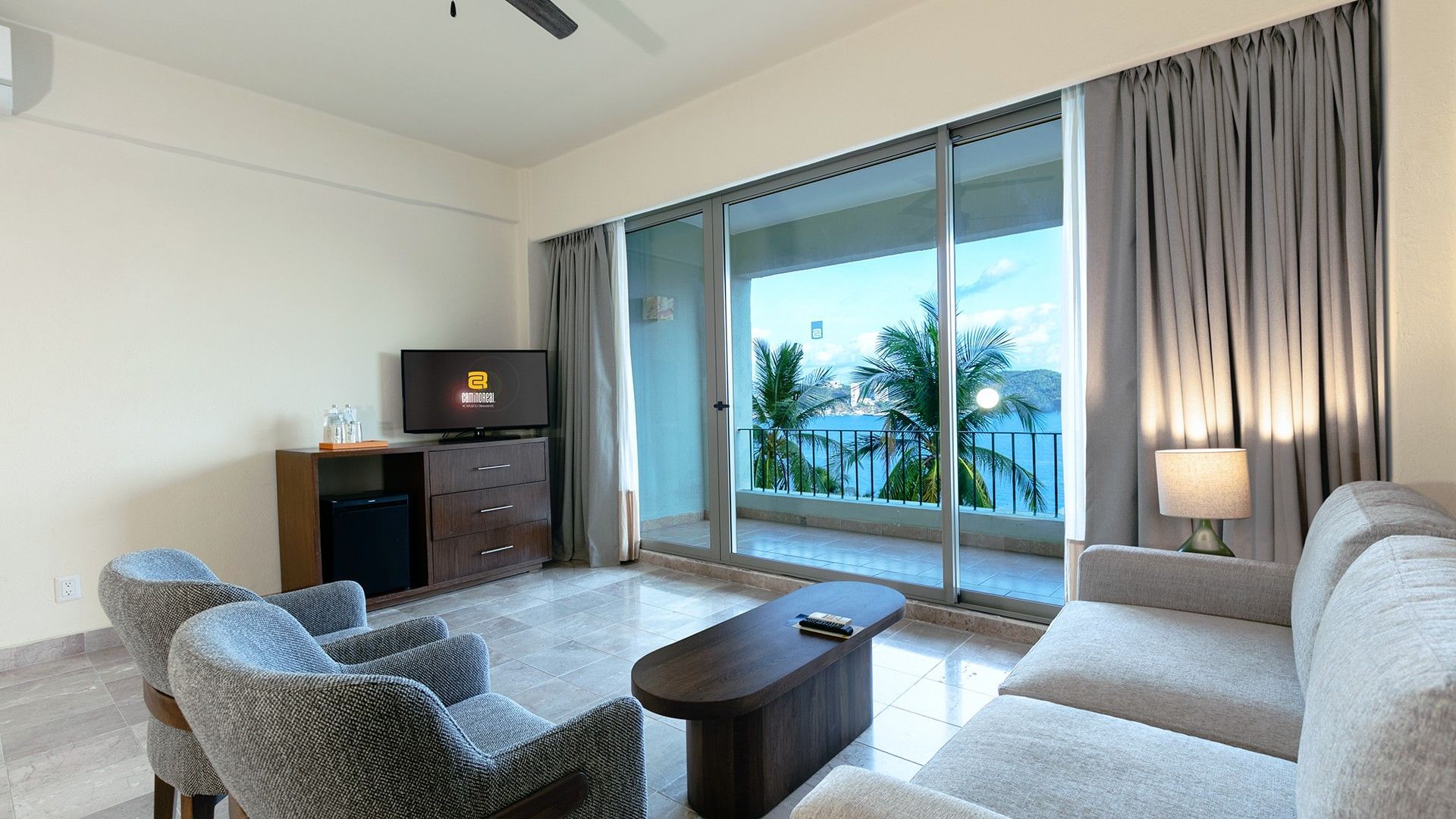 King Master Suite living area with a TV, dark wood dresser, and a balcony view of palm trees at Camino Real Acapulco Diamante