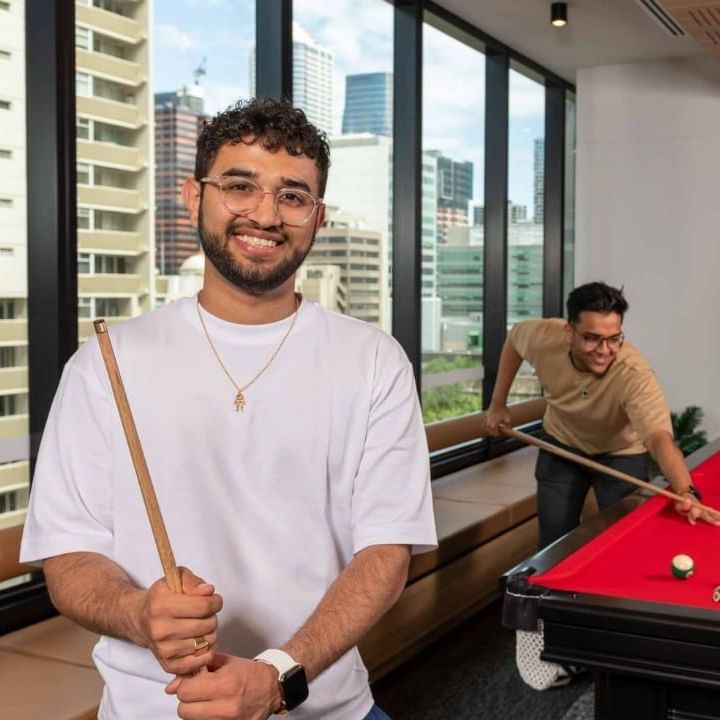 Residents playing pool in an office lounge with a cityscape view.