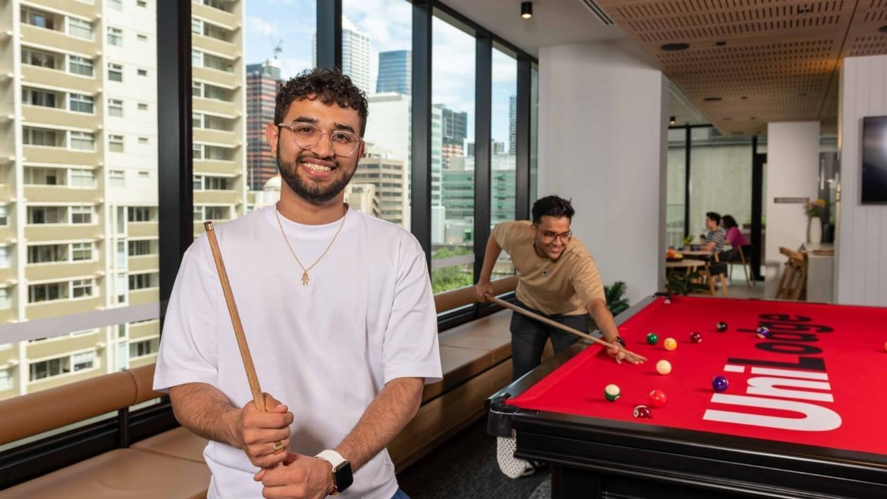 Residents playing pool in an office lounge with a cityscape view.