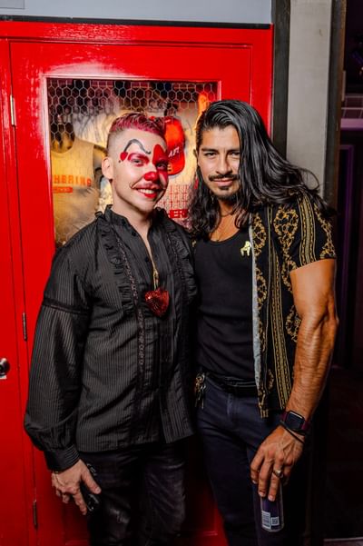 Two men pose together in front of a vibrant red door, showcasing stylish outfits at The Gaythering