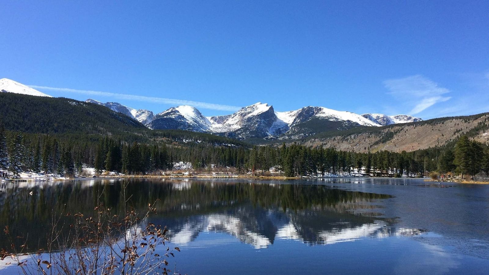 Snowy peaks by a pine forest reflecting in a clear lake under a blue sky at Warwick Denver