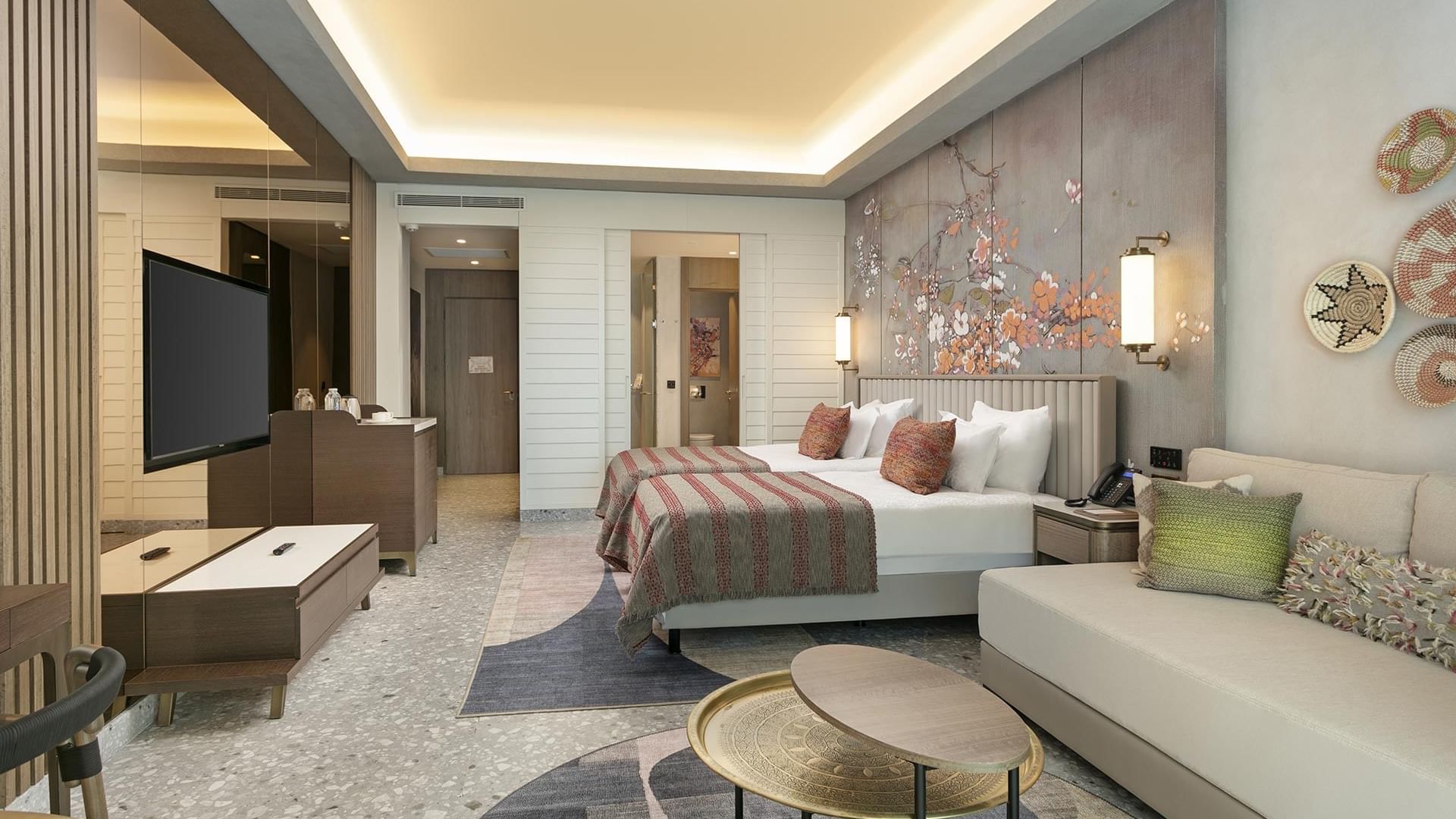 Wall art behind double beds, TV & a seating area with a sofa in Superior Room Golf View at Cullinan Belek