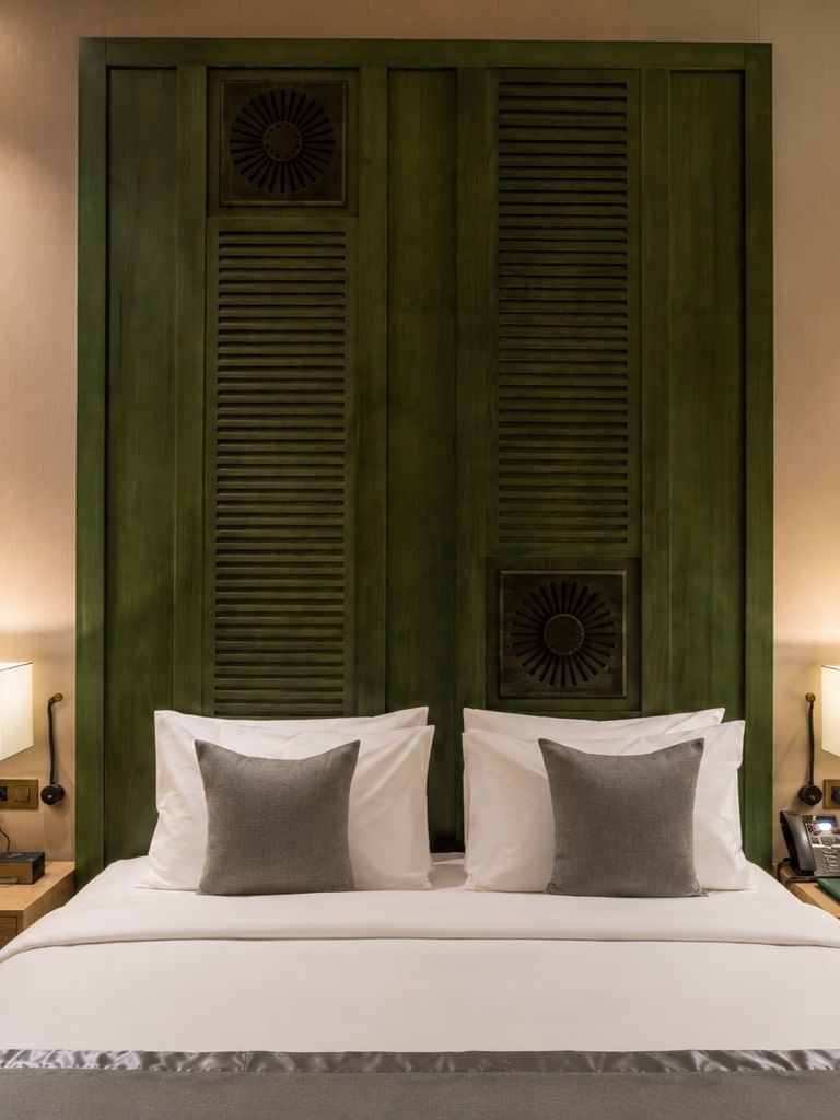 Bed beneath wood-paneled headboard between table lamps in Deluxe Skyline View at Naviti by Warwick Jeddah