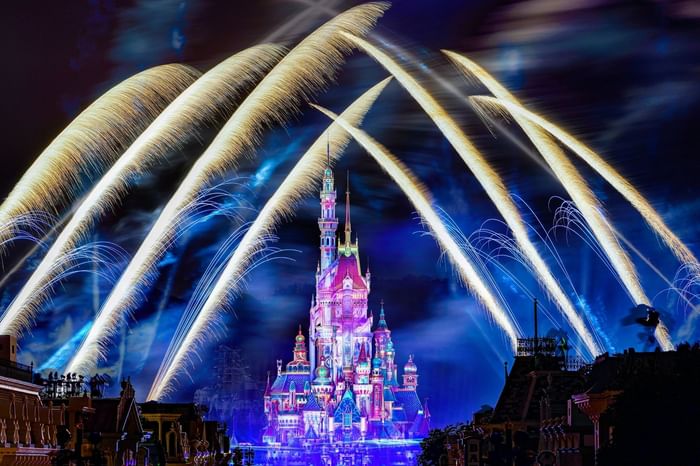 Nighttime fireworks over a fairy tale castle with blue and pink lights at Park Hotel Group