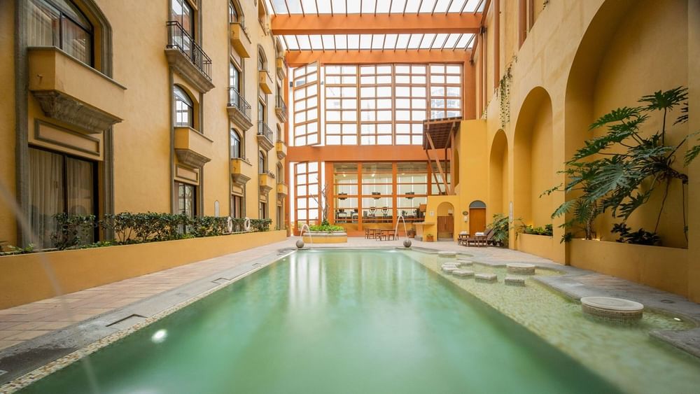 Serene indoor lap pool housed in a bright atrium with yellow walls and arches at Quinta Real Monterrey