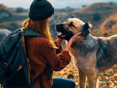 Girl wearing a beanie & backpack petting her dog on the mountains near ElDorado, a Coast Hotel