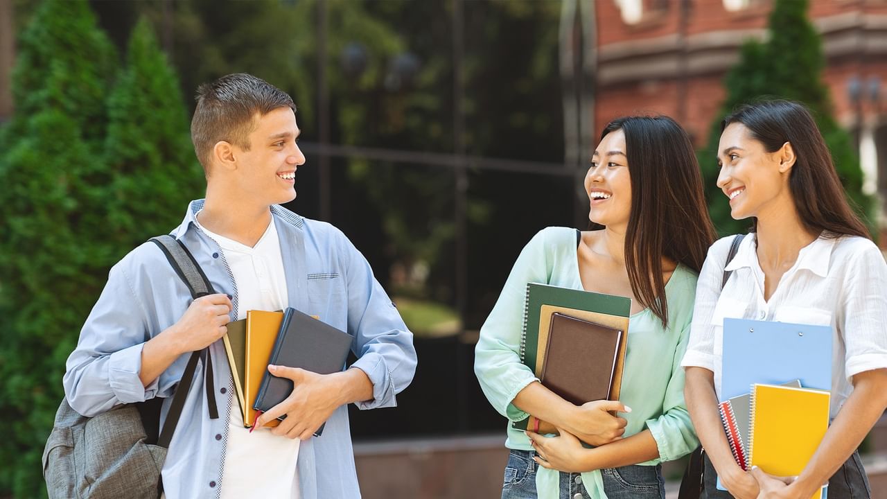 Three smiling students carrying notebooks and backpacks walk together on campus