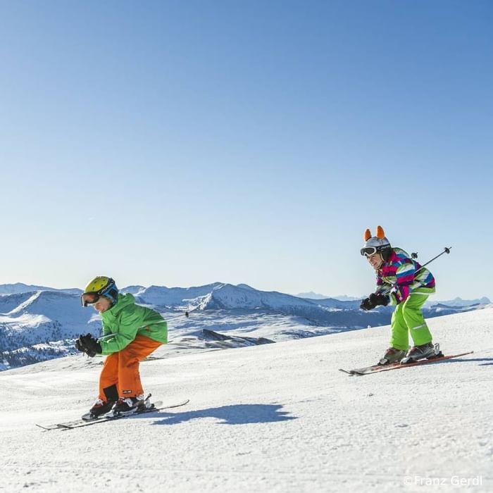 Two children skiing down a mountain near Falkensteiner Hotels