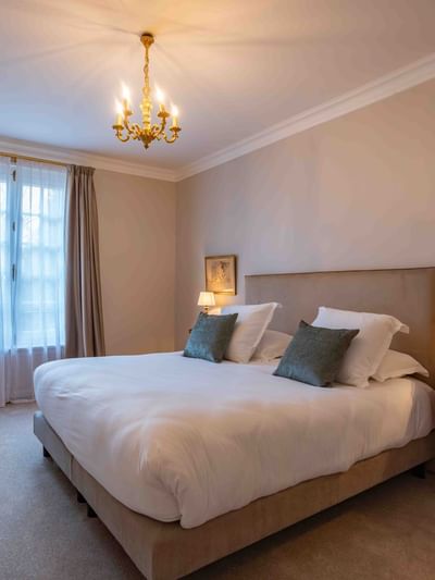 Chambre élégante avec lit, chaise bleue, lustre, et lampes de chevet sur table en bois.