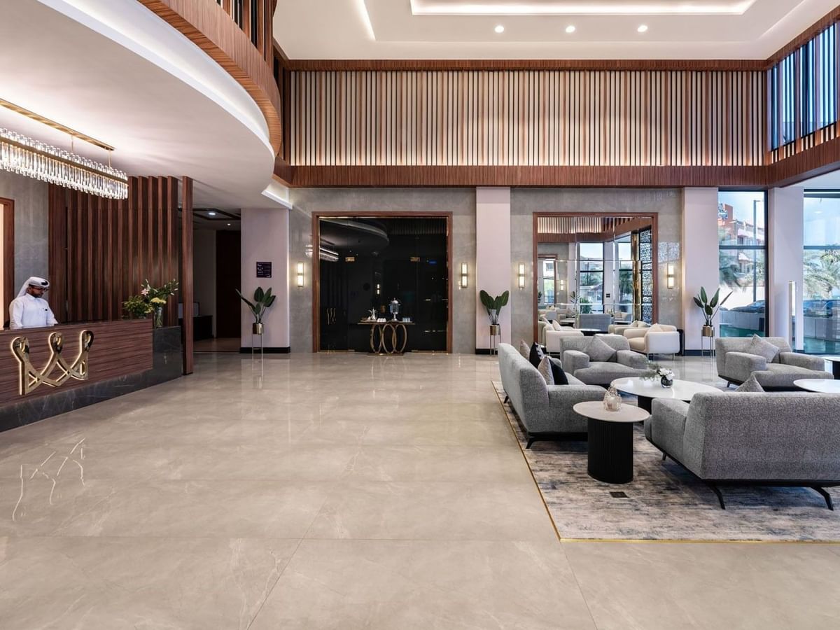 Spacious lobby at Warwick Al Jubail with grey sofas on a rug by a wooden reception desk under a tiered ceiling