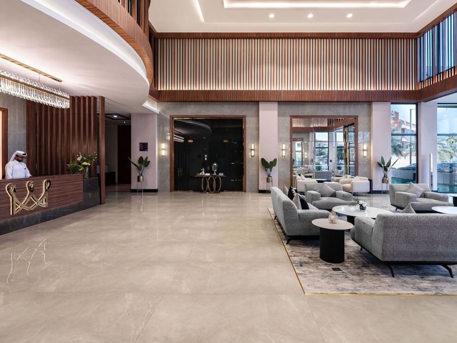 Spacious lobby at Warwick Al Jubail with grey sofas on a rug by a wooden reception desk under a tiered ceiling