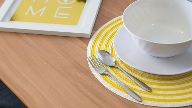 Wooden table set with white bowl, yellow striped placemat, cutlery, glass, and succulent plant at StudentLiving - on Margaret