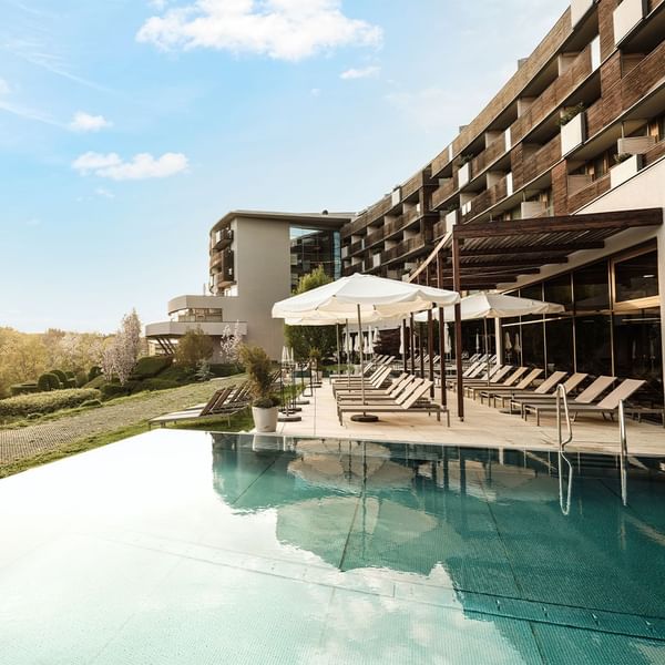 Piscina esterna e lettini sotto gli ombrelloni di un hotel moderno at Falkensteiner Group