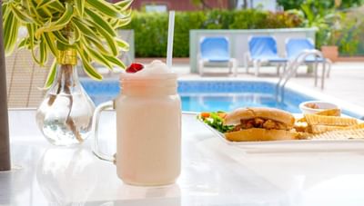 Frosted smoothie jar with straw beside burger & fries with pool view in Hott Pott Restaurant at Worthing Court Apartment