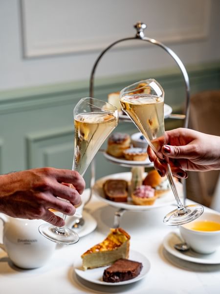 Deux personnes trinquant avec des coupes de champagne lors d'un goûter à l'Hôtel Westminster, à Paris.