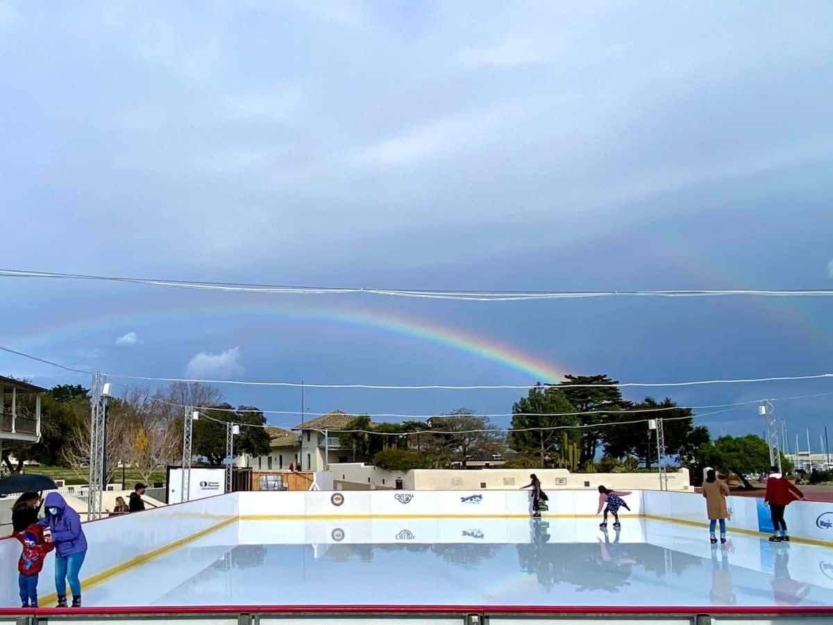 A rainbow over an outdoor ice rink with people skating.