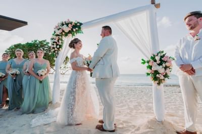 Joyful couple exchanging vows at a beach wedding ceremony under a floral arch near Amsterdam Manor Beach Resort