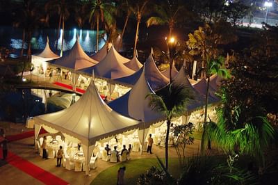 Elegant tents with tables by a calm lake, lit at night and surrounded by palms at The Saujana Hotel Kuala Lumpur
