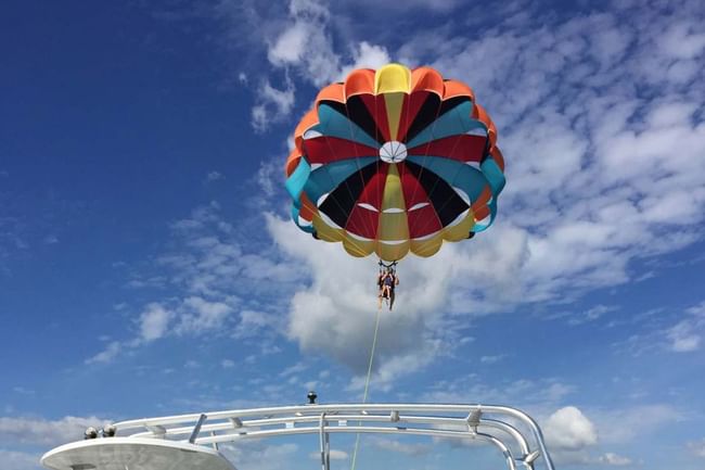 A vibrant, multi-colored parasail canopy soaring through a blue sky with white clouds at Shangri-La Resort and Golf Club