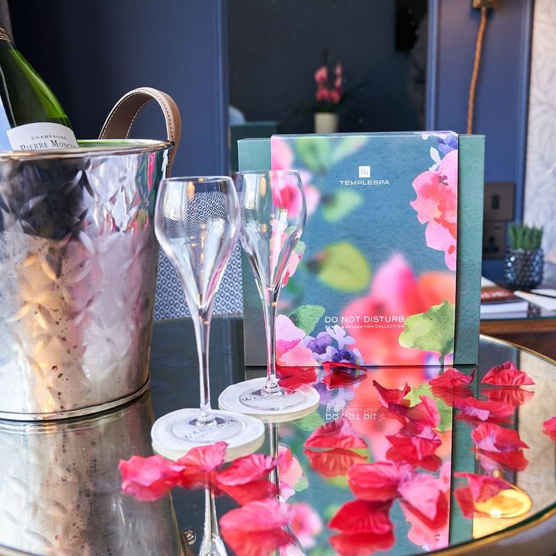 Champagne bucket with two glasses and floral menu on a table with petals at The Capital Valentines Experience.