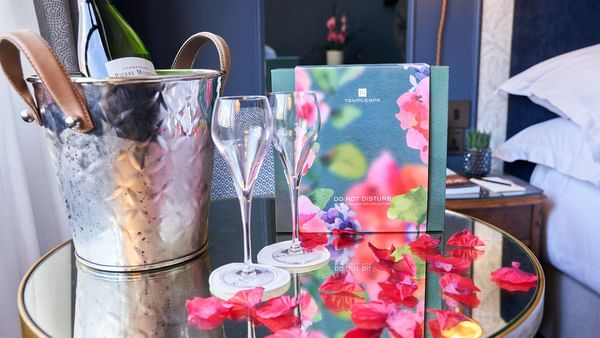Champagne bucket with two glasses and floral menu on a table with petals at The Capital Valentines Experience.