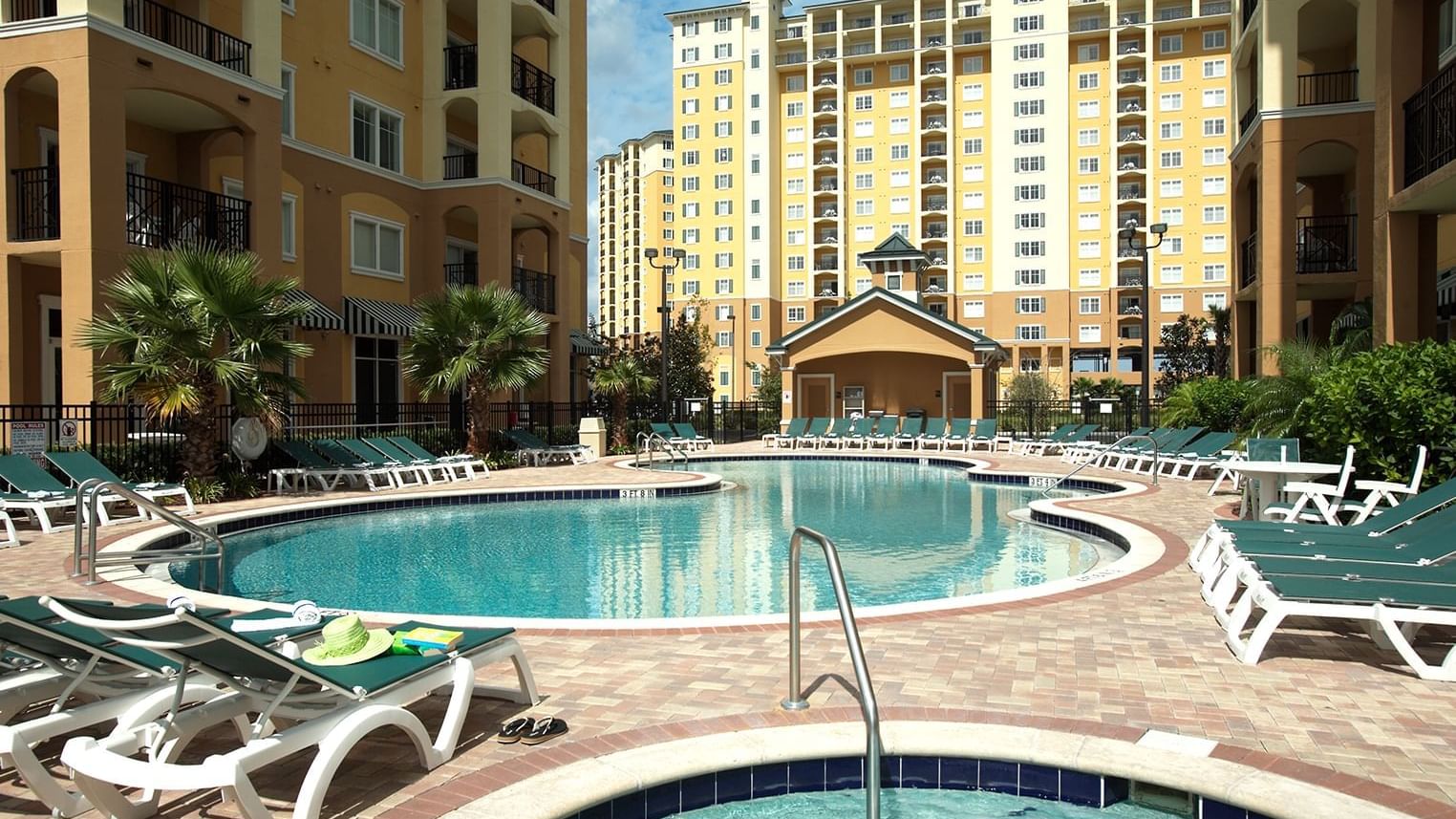 A large pool with lounge chairs and palm trees in front of a multi-story building.