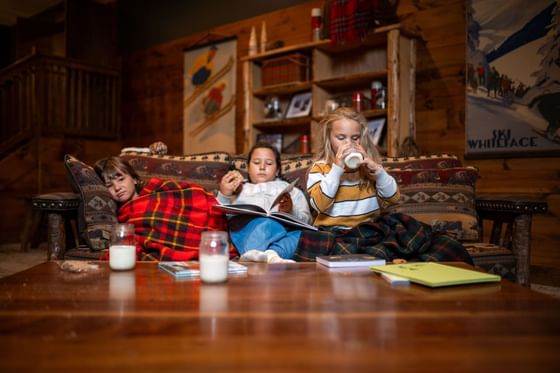 Two children reading a book and one child sleeping on a couch in The Lodge at Schroon Lake