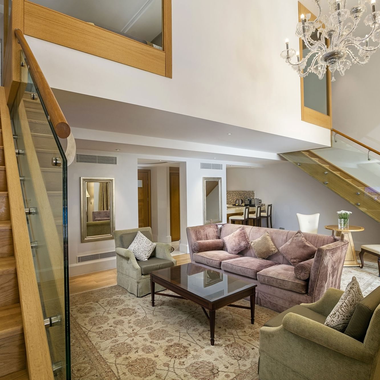 Erstklassige Pool-Duplex-Suite im Titanic Mardan Palace – Wohnzimmer mit Treppe, Kronleuchter, Plüschsesseln und Glasgeländer.