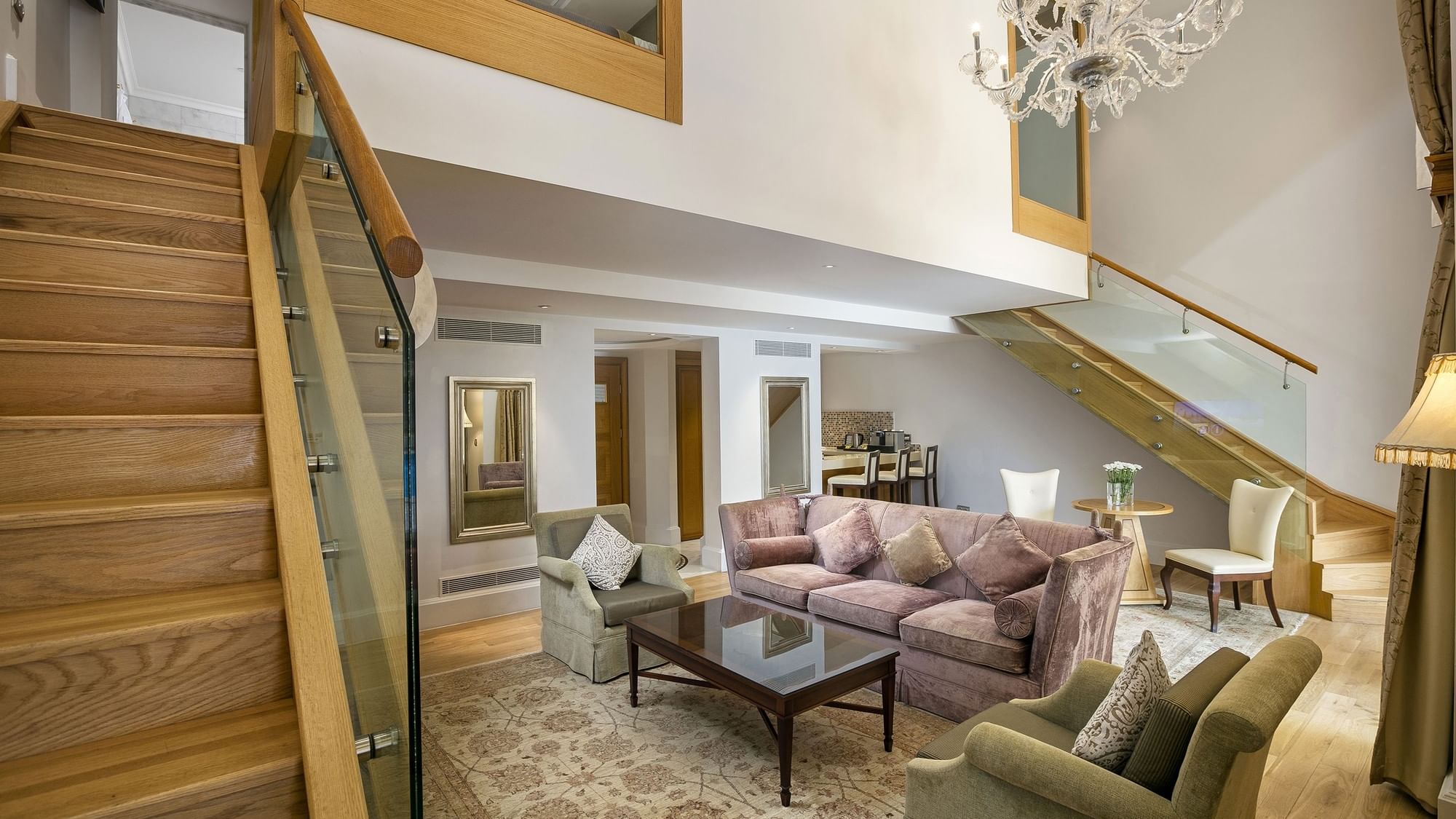 Erstklassige Pool-Duplex-Suite im Titanic Mardan Palace – Wohnzimmer mit Treppe, Kronleuchter, Plüschsesseln und Glasgeländer.