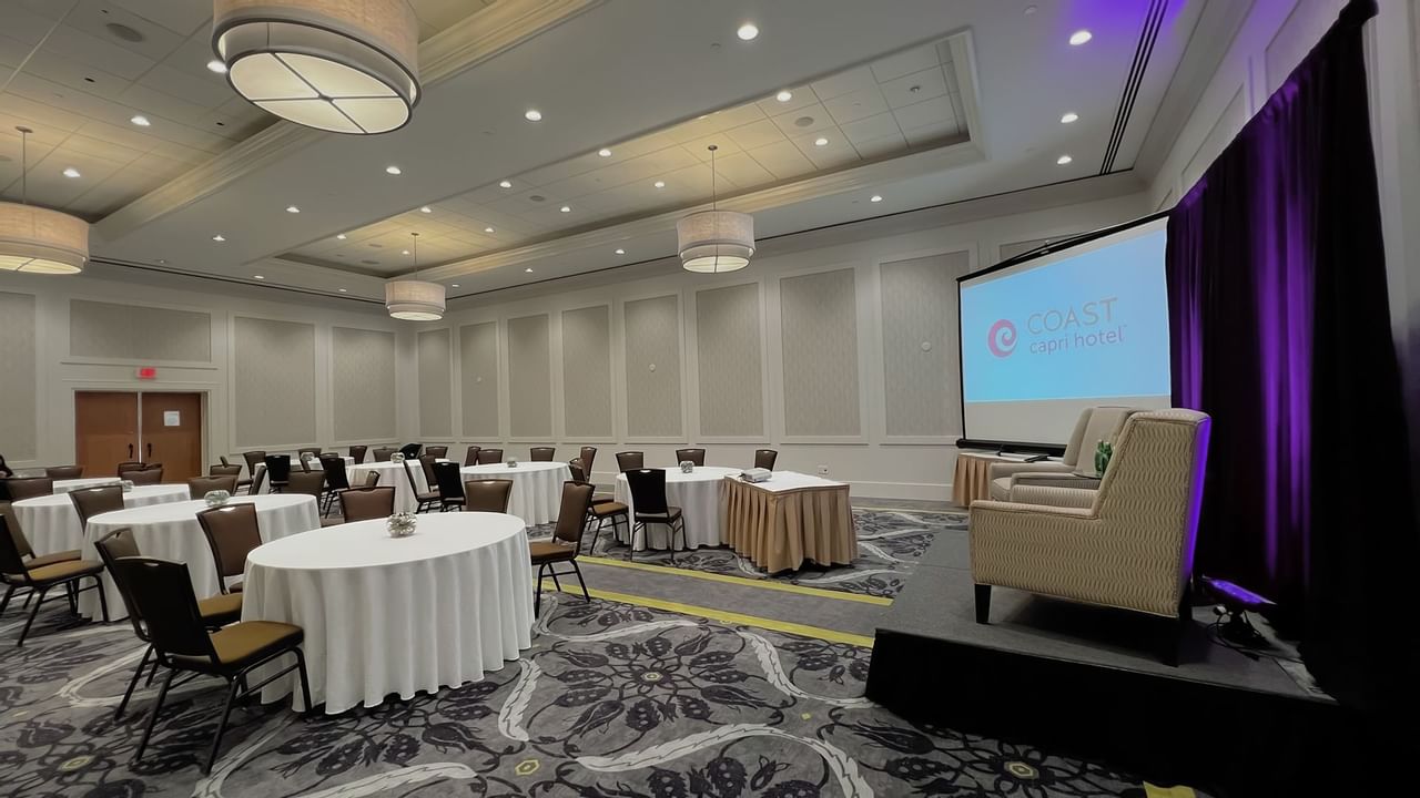 Ballroom with round tables, chairs, stage, podium and presentation screen