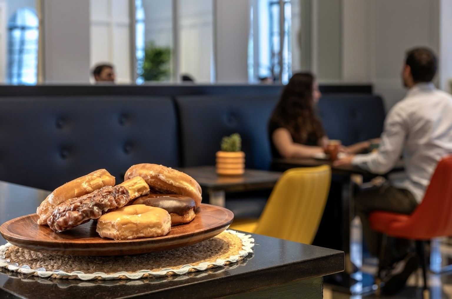 Wooden plate of donuts, placed by a booth seating area with guests at cafe in Warwick Allerton Chicago
