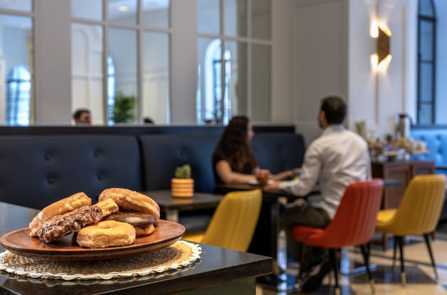 Wooden plate of donuts, placed by a booth seating area with guests at cafe in Warwick Allerton Chicago