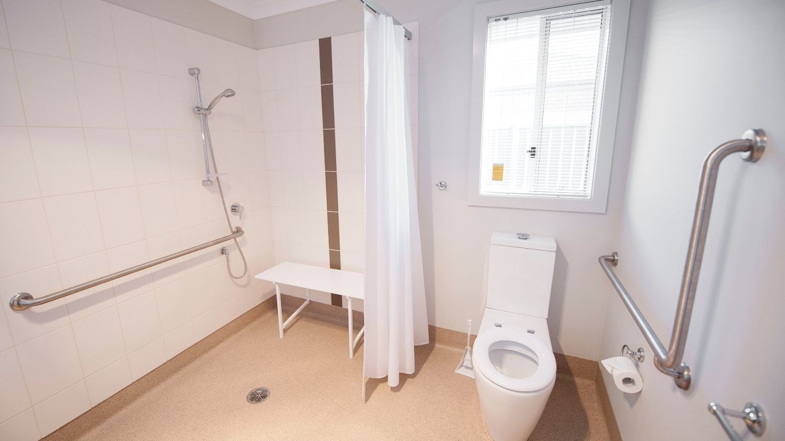White accessible bathroom with shower, toilet, and grab bars at La Trobe University Regional Housing.