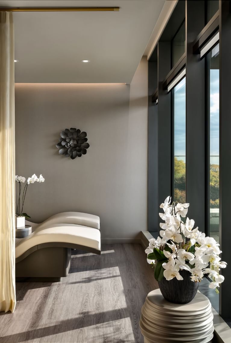Curved white treatment beds by a window with orchids and a stone sculpture, overlooking greenery at Hotel X Toronto