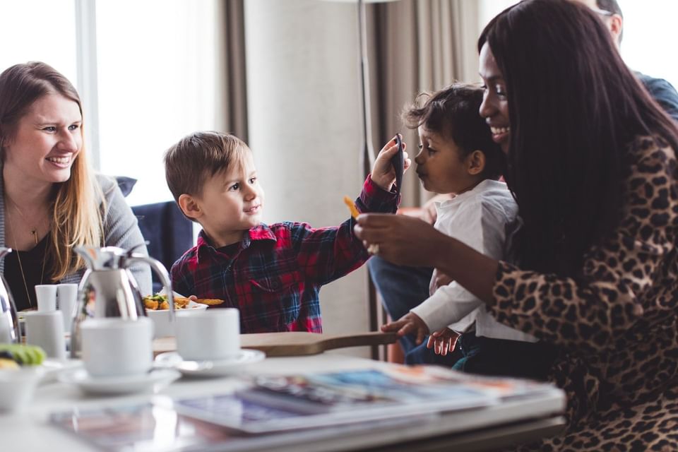 Family enjoying breakfast spread with coffee and pastries near large bright room window at Hotel X Toronto