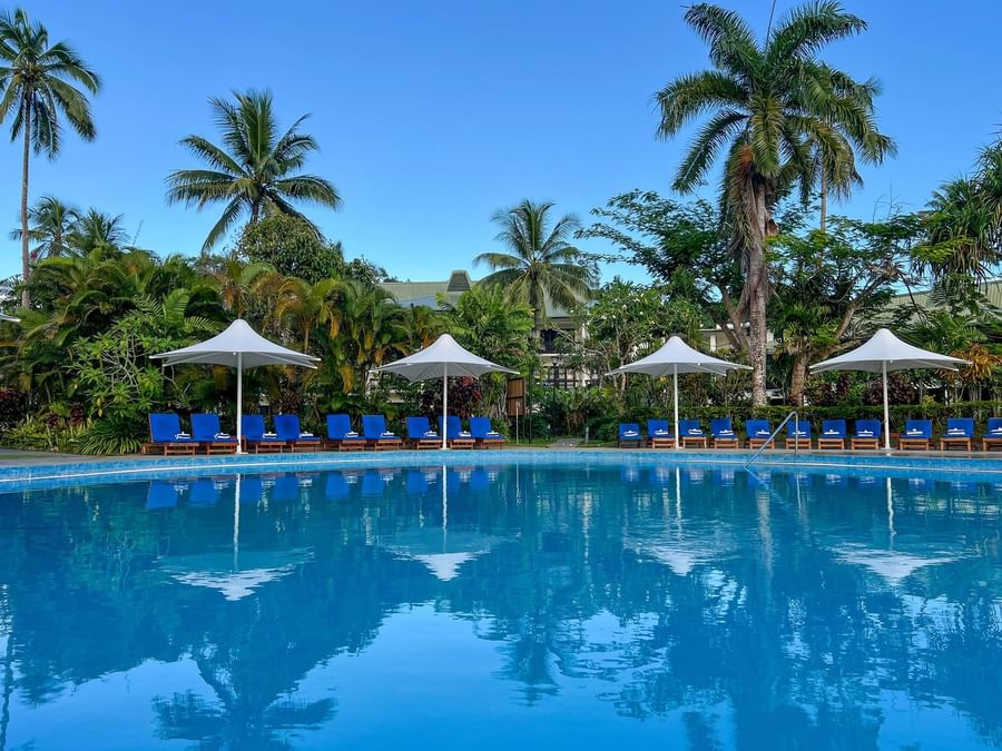 Blue pool with lounge chairs under white umbrellas at The Naviti Resort - Fiji.