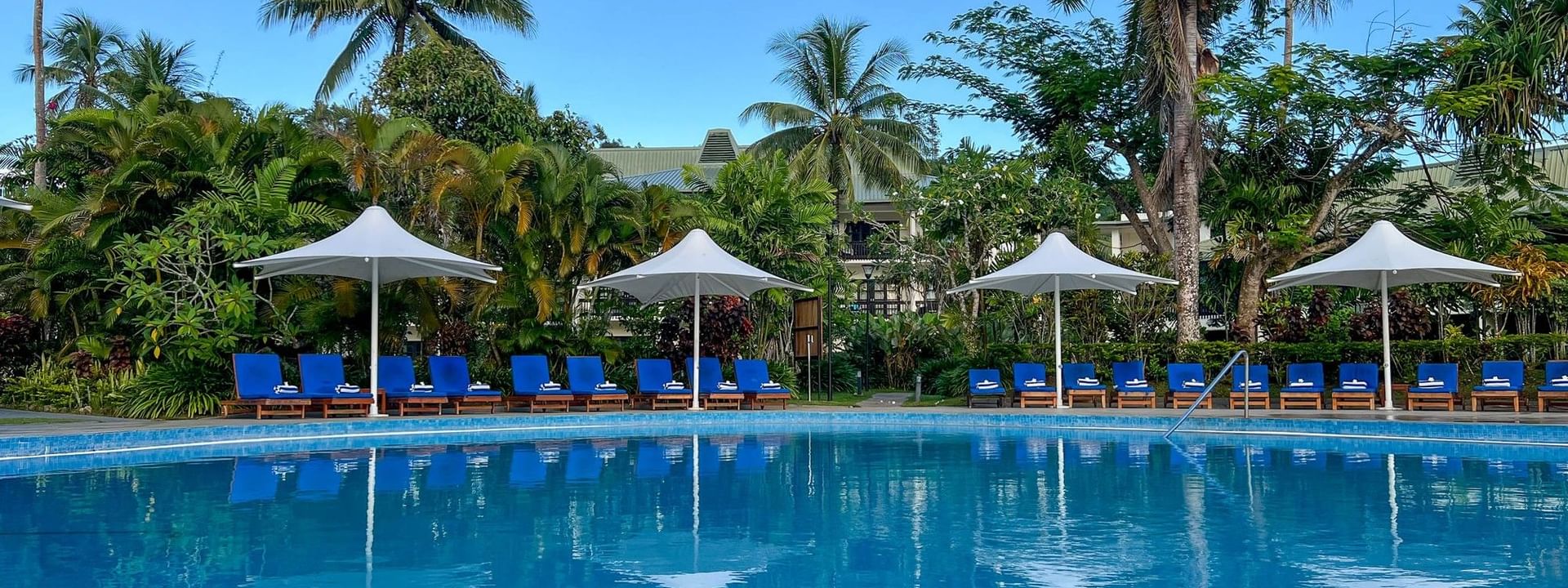 Swimming pool with lounge chairs under umbrellas at The Naviti Resort, Korolevu