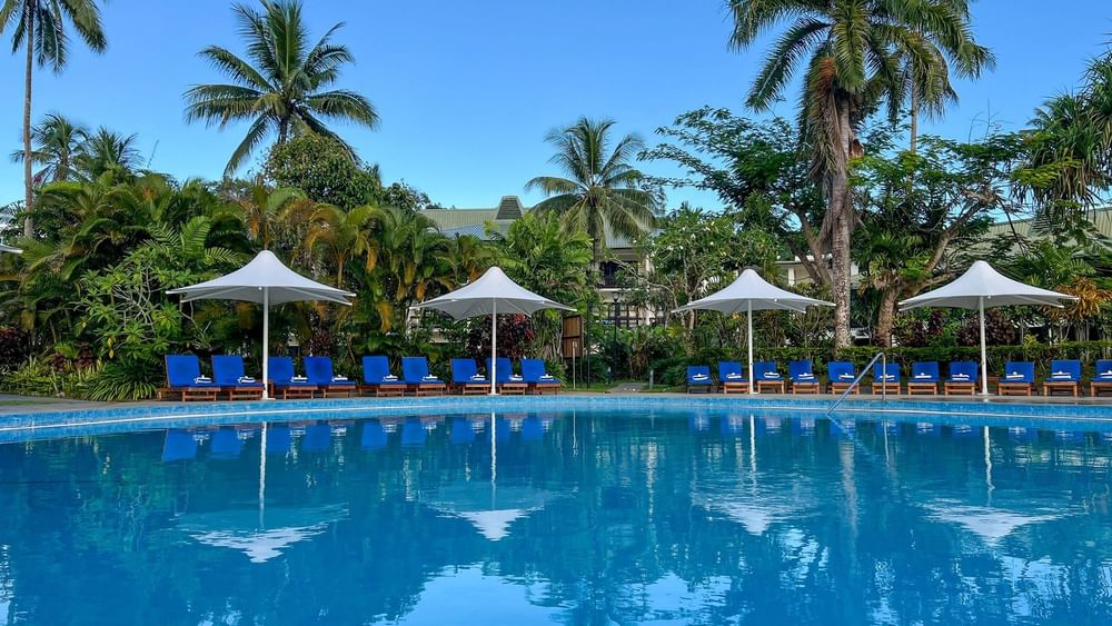 Swimming pool with lounge chairs under umbrellas at The Naviti Resort, Korolevu.
