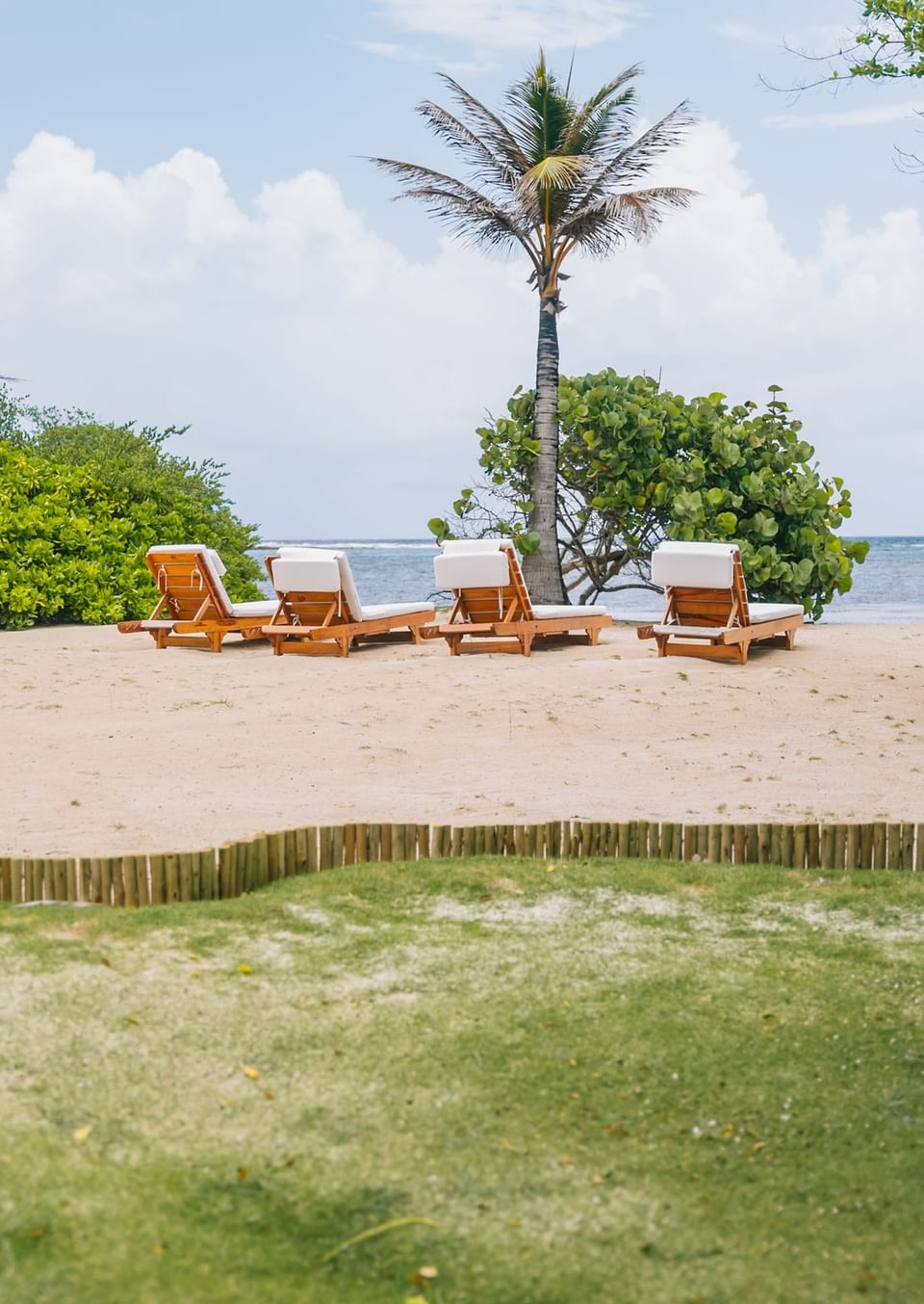 Four wooden lounge chairs with white cushions on the beach at Barefoot Cay Resort & Marina