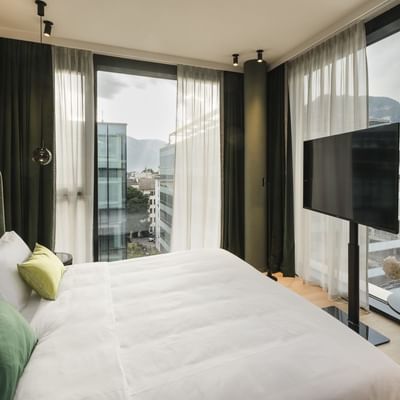 Hotelzimmer mit großem Bett, Fernseher, und Panoramablick auf Stadt und Berge.