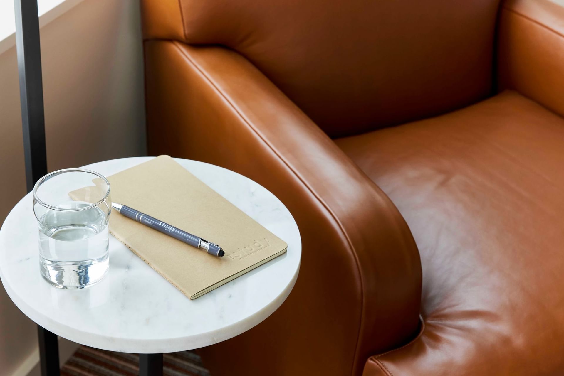 A notepad and a pen with a glass of water by a leather cushioned lounger in The Study Hotel at Johns Hopkins