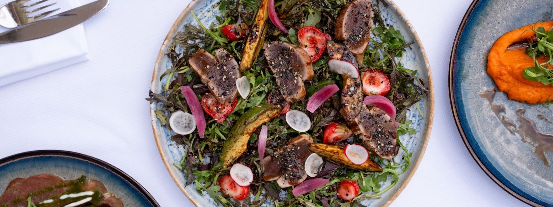 Seared tuna slices on a bed of greens by radish on a plate in Seminars & Banquets at Warwick Paris Champs Elysées