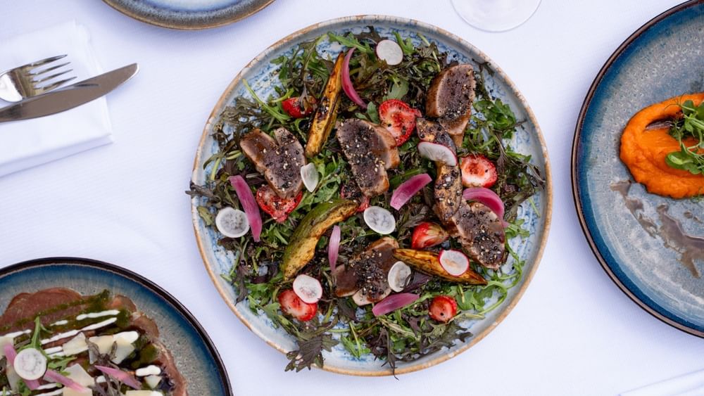 Seared tuna slices on a bed of greens by radish on a plate in Seminars & Banquets at Warwick Paris Champs Elysées