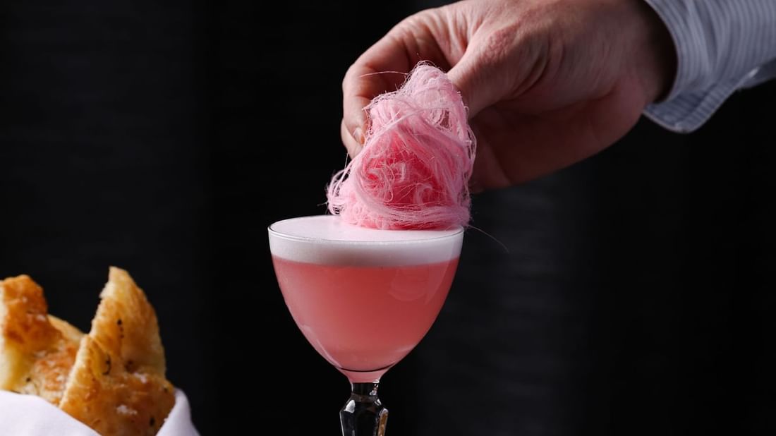 Hand placing pink cotton candy atop a cocktail in Boulevard Brasserie & Bar at Novotel Sydney Olympic Park
